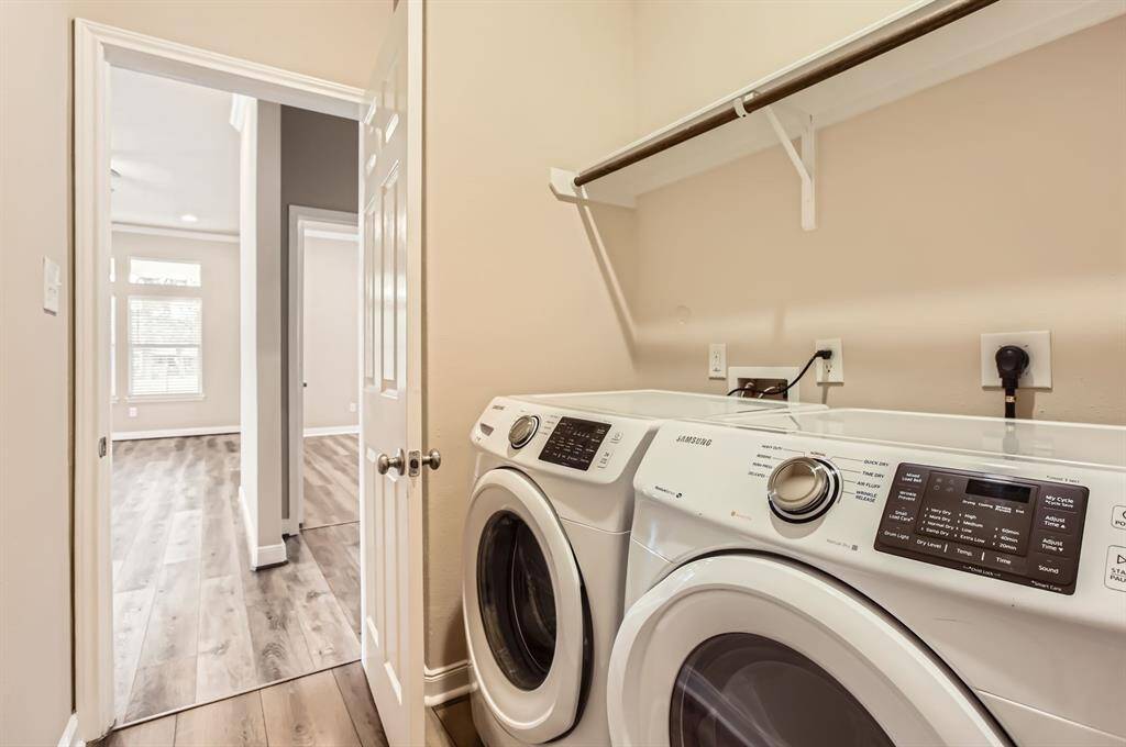 This laundry room equipped with a Samsung washer and dryer. It features beige walls and a shelf above the appliances for storage.