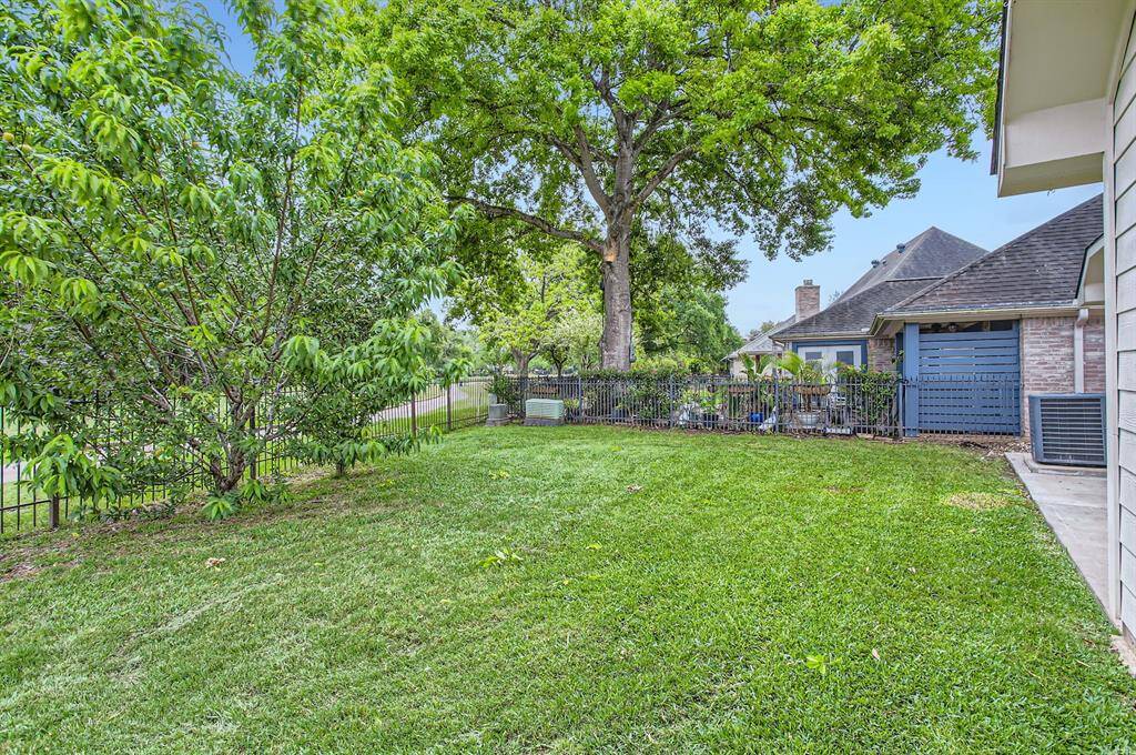 A spacious backyard with well manicured lawn, mature trees, and a metal fence. Ideal for families or pets, it offers a blend of sun and shade.
