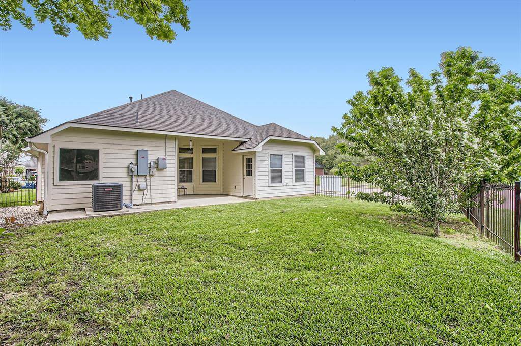 The backyard with a well-maintained lawn, a covered patio, and a fenced boundary.