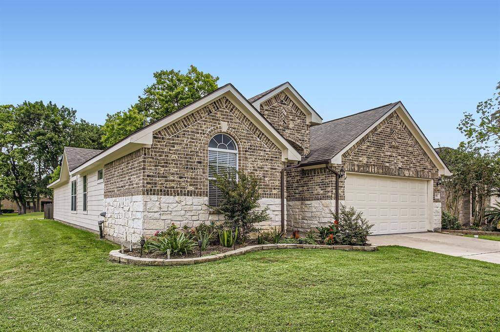 Single-story home with a brick and stone exterior, featuring a well-maintained lawn and landscaped flower beds. The arched window adds character, and the two-car garage offers convenience. Situated in a neighborhood with mature trees.