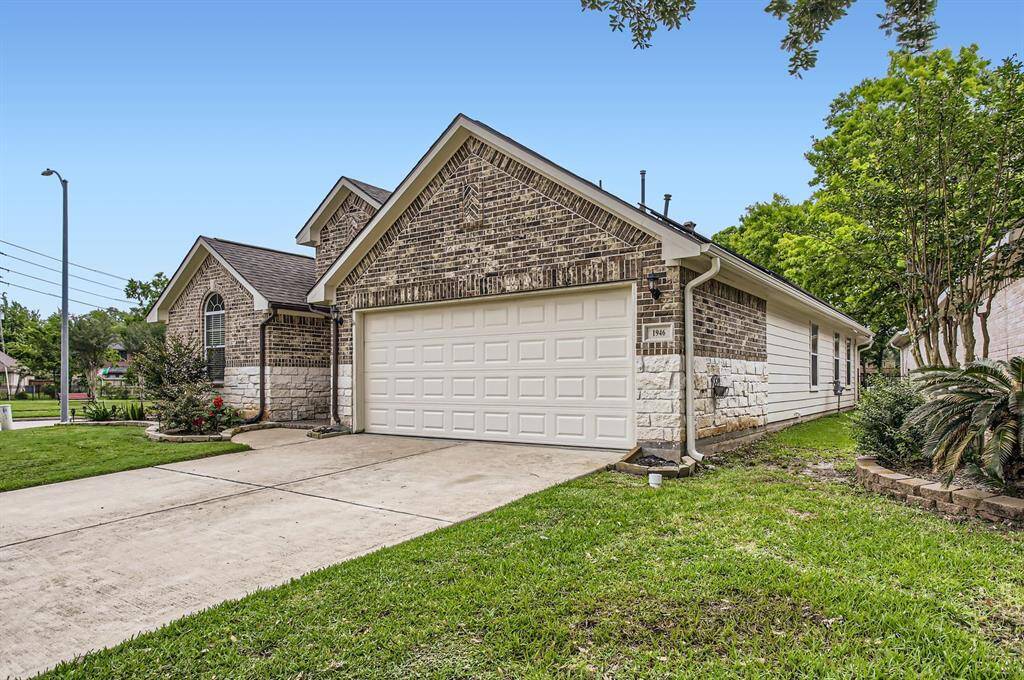 This photo showcases side view of this brick and stone single-story home with a two-car garage. It features a well-maintained front lawn with landscaped greenery.