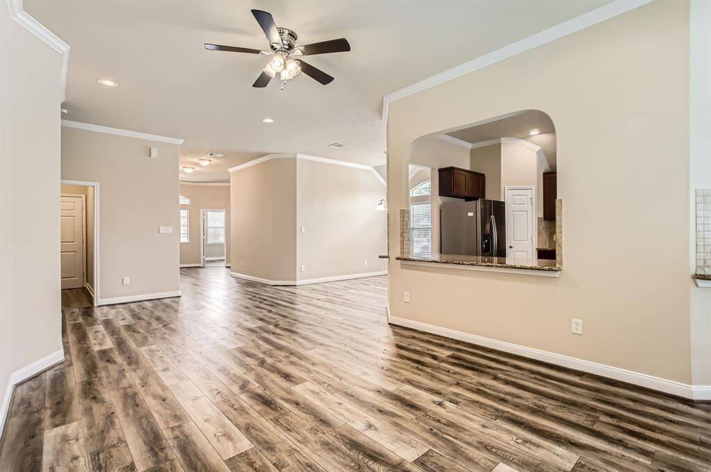 Spacious open-concept living area features beautiful wood flooring, neutral walls, and a ceiling fan. The kitchen has granite countertops and stainless steel appliances, visible through a wide, arched pass-through. Ideal for modern living and entertaining.