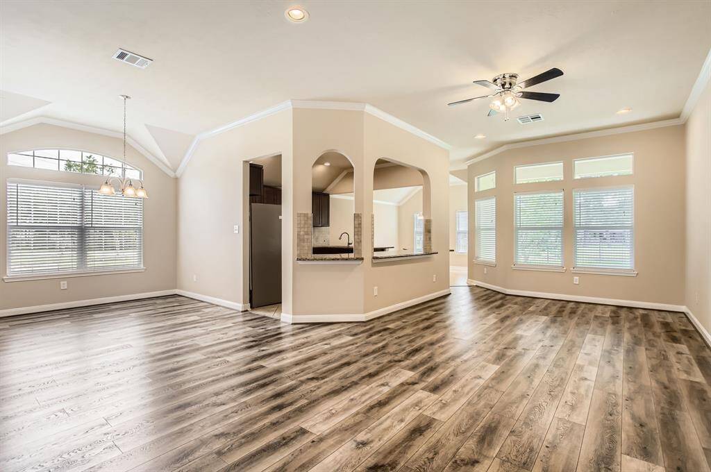 This spacious open-concept living area features wood flooring, abundant natural light from large windows, and a cozy kitchen nook with a modern ceiling fan. Perfect for entertaining and family gatherings.