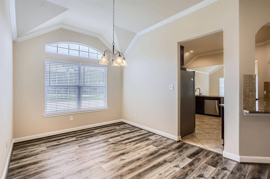 Bright dining area with large window, elegant light fixture, and wood flooring. Adjacent to a modern kitchen featuring stainless steel appliances and tiled floors.