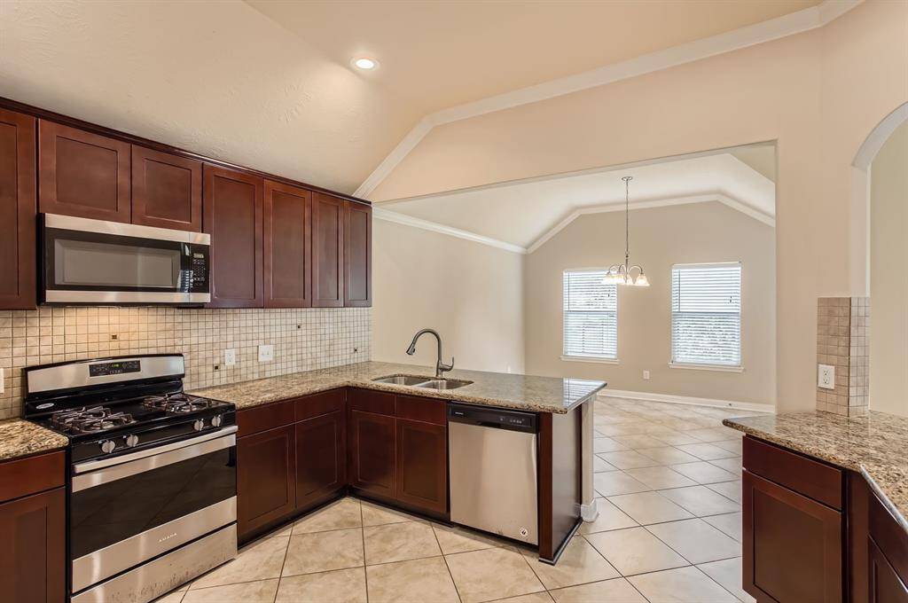 This kitchen features sleek dark wood cabinetry, stainless steel appliances, and granite countertops. It opens to a bright dining area with large windows and tiled flooring, creating a spacious and modern feel.