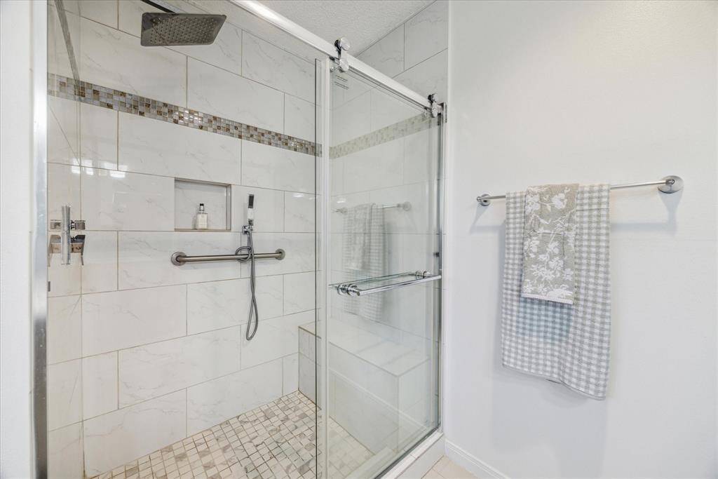 A walk-in shower with glass enclosure has tile accents that offers convenient storage and seating.