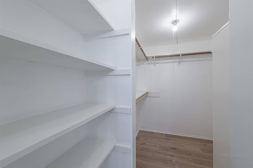 The walk-in closet is opposite the vanity.  The luxury vinyl plank flooring is reprised.  Built in shelving and several hanging racks offer plenty of storage space.