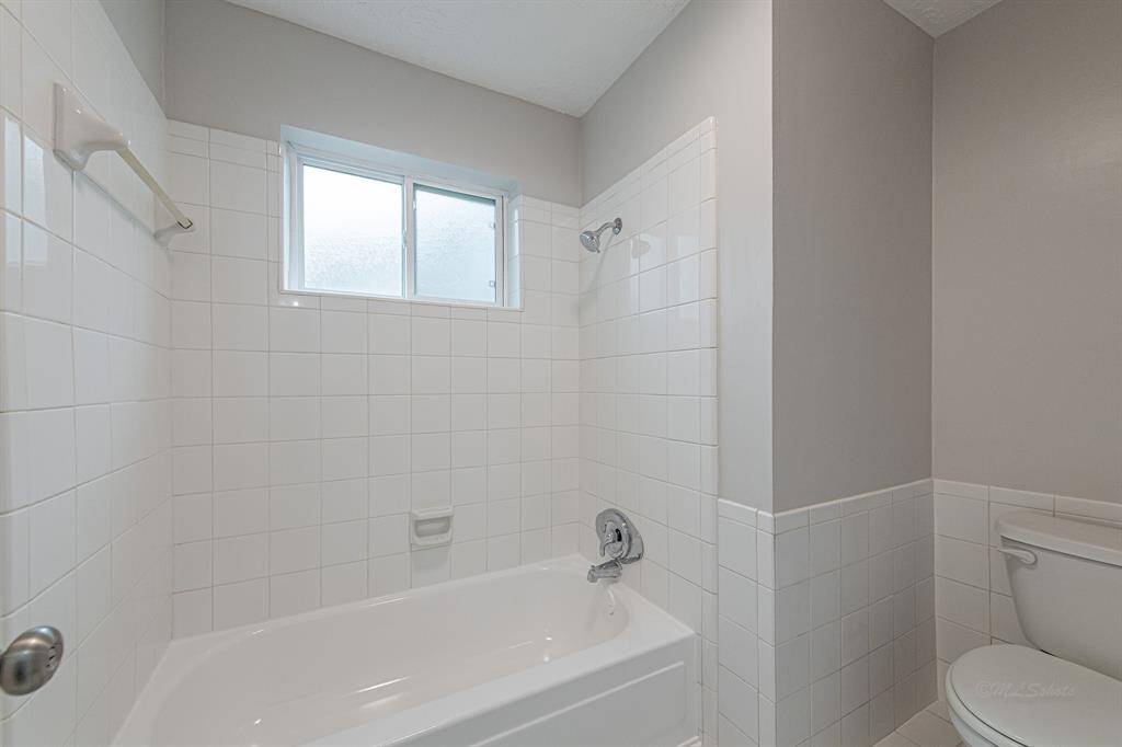 The tub, shower, and commode are tucked behind a door for privacy.  Natural light flows throuhg a double pane transom window.  The iron tub has been freshly resurfaced.  The crisp white tile surround extends behind the commode and complements the tile on the floor.