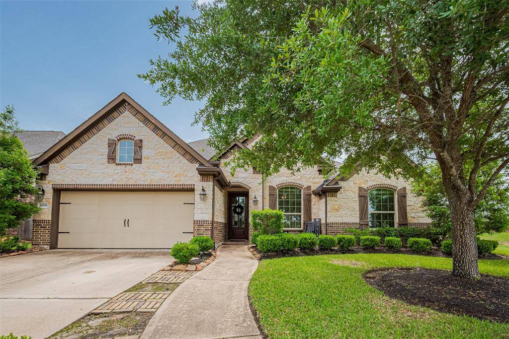 A graceful brick façade anchors the front of the home, complemented by manicured landscaping and a mature tree that adds character and shade. A walkway guides you toward the recessed entry, while thoughtfully arranged plant beds soften the architectural lines and add vibrant curb appeal.