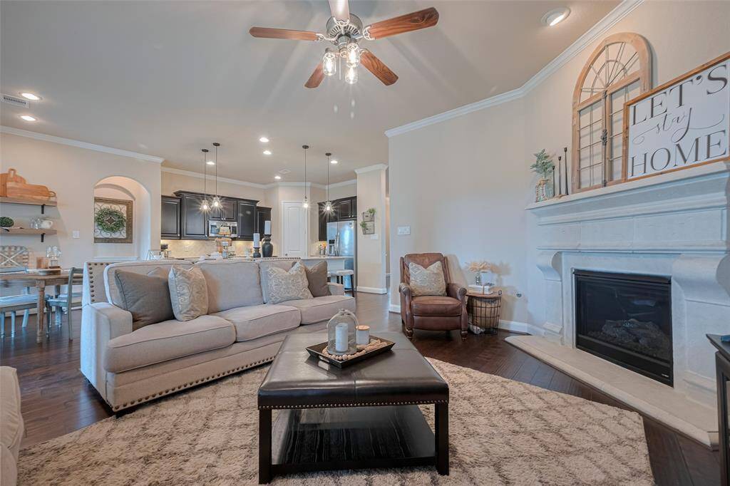 Spacious yet welcoming, the living room centers around a fireplace that adds warmth and visual interest. Towering windows frame views of the outdoors, while a ceiling fan ensures year-round comfort. The open layout flows seamlessly into the kitchen and breakfast area.