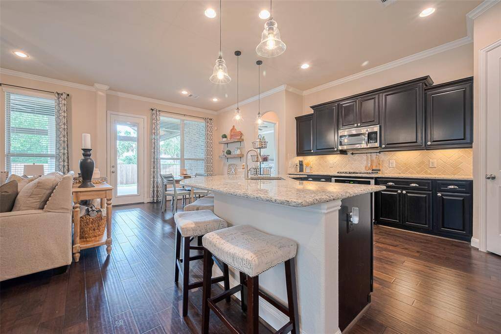 The kitchen is both functional and stylish, anchored by a generous island with an integrated sink and bar seating. Pendant lighting highlights the workspace, while dark cabinetry contrasts against a luminous backsplash, enhanced by subtle under-cabinet lighting. Ideal for gatherings or quiet mornings.
