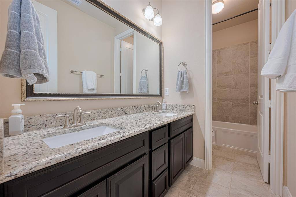 This shared bathroom offers comfort and function, with an expansive dual-sink vanity and a separate grooming area. A broad mirror and soft lighting create a polished and calming feel.