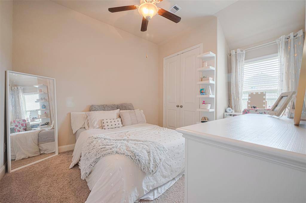A spacious, carpeted retreat bathed in sunlight from a large window. Soft neutral tones and a ceiling fan enhance comfort, while the closet offers plenty of storage.