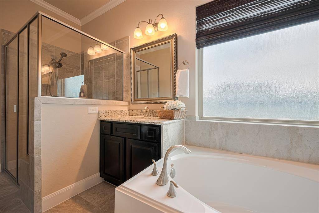 Designed for relaxation, the en suite bathroom includes a deep soaking tub set beneath a frosted window, flanked by twin vanities. A glass-enclosed shower adds a sleek, modern touch to this well-appointed space.