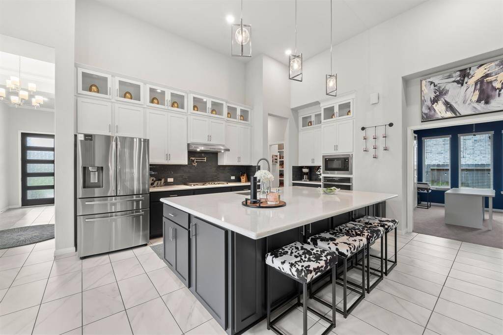 This amazing kitchen includes tall cabinets with display windows on top, a massive island with a breakfast bar and extra storage, quartz countertops, higher end GE Profile appliances, and high ceilings.