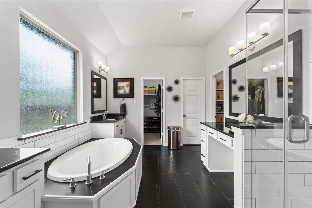 The striking primary bathroom includes separate oversized shower and soaking tub, two separate sinks with storage and an additional vanity area next to the shower.