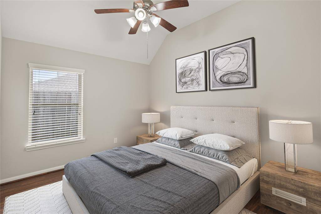 This bedroom features vaulted ceilings, a window that allows natural light to pour in, and sleek laminate flooring, creating an airy and modern living space.