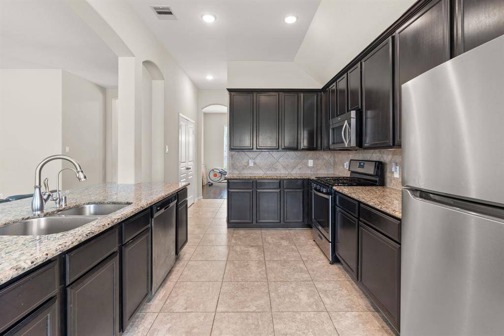 The kitchen boasts dark stained brown cabinets, a kitchen island equipped with a sink and dishwasher, and vaulted ceilings, combining functionality with spaciousness for a stylish culinary haven.