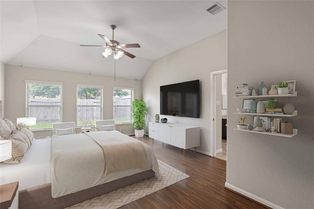 The primary bedroom boasts vaulted ceilings, three large windows that flood the room with natural light, and sleek laminate flooring, creating a spacious and elegant retreat.