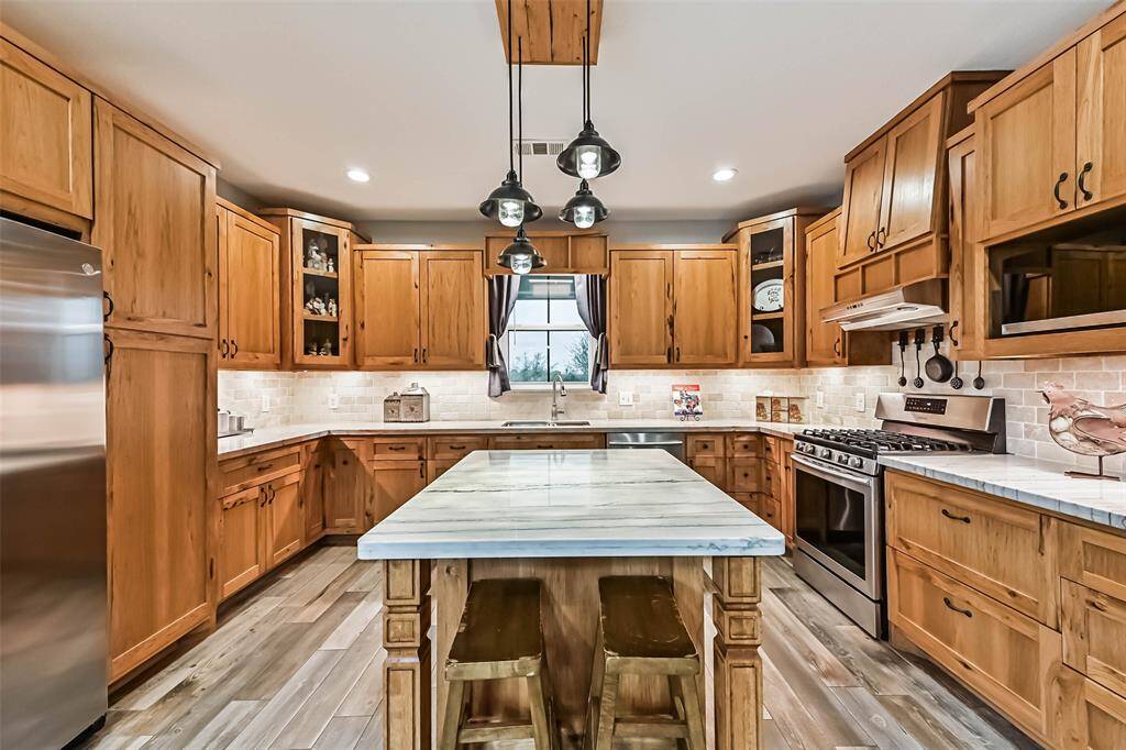 Chef's eat-in island kitchen features custom hickory cabinets, designer backsplash, lengthy quartz countertops, stainless steel appliances and under cabinet lighting