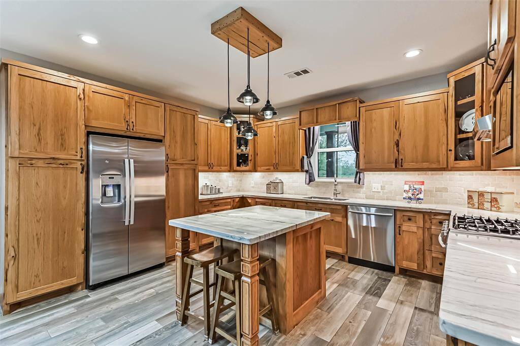 Chef's eat-in island kitchen features custom hickory cabinets, designer backsplash, lengthy quartz countertops, stainless steel appliances and under cabinet lighting