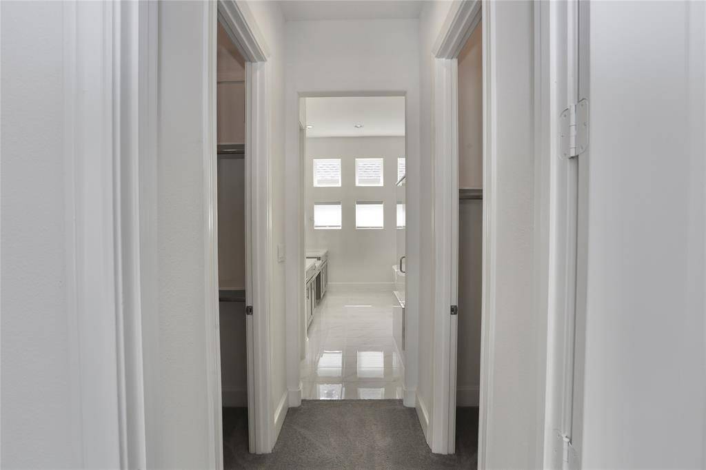 Hallway from primary bedroom to primary bathroom. 2 walk-in closets on either side.