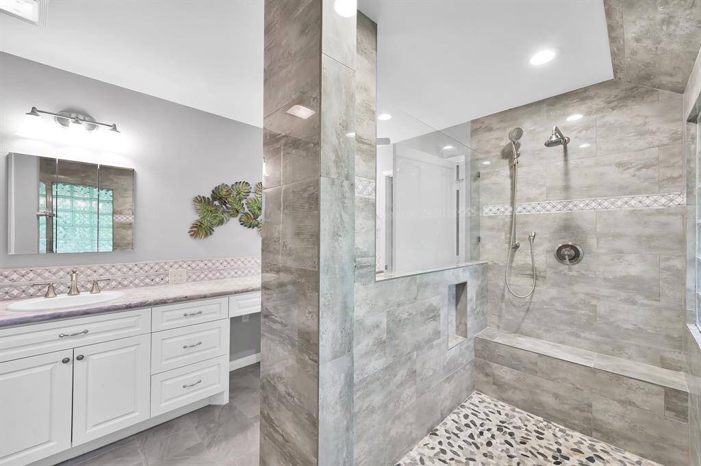 View of large walk in shower with bench, area for toiletries and multiple shower heads.