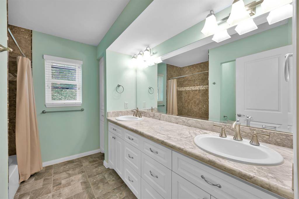 Secondary bathroom with double sinks tub shower combo and extra cabinetry.