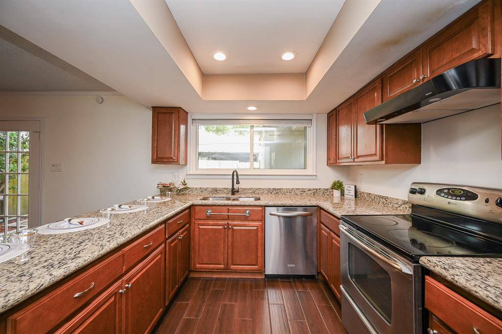 This kitchen features granite countertops, stainless steel appliances, and warm wood cabinetry. It has a modern feel with recessed lighting and a window above the sink that provides natural light.