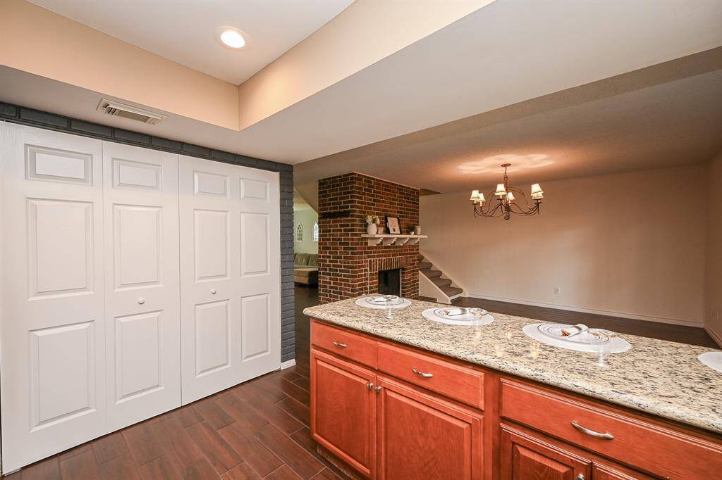 This inviting space features a cozy brick fireplace, a stylish chandelier, and a granite countertop with wooden cabinetry. The open layout is enhanced by warm wood flooring and ample closet space. Perfect for comfortable living and entertaining.