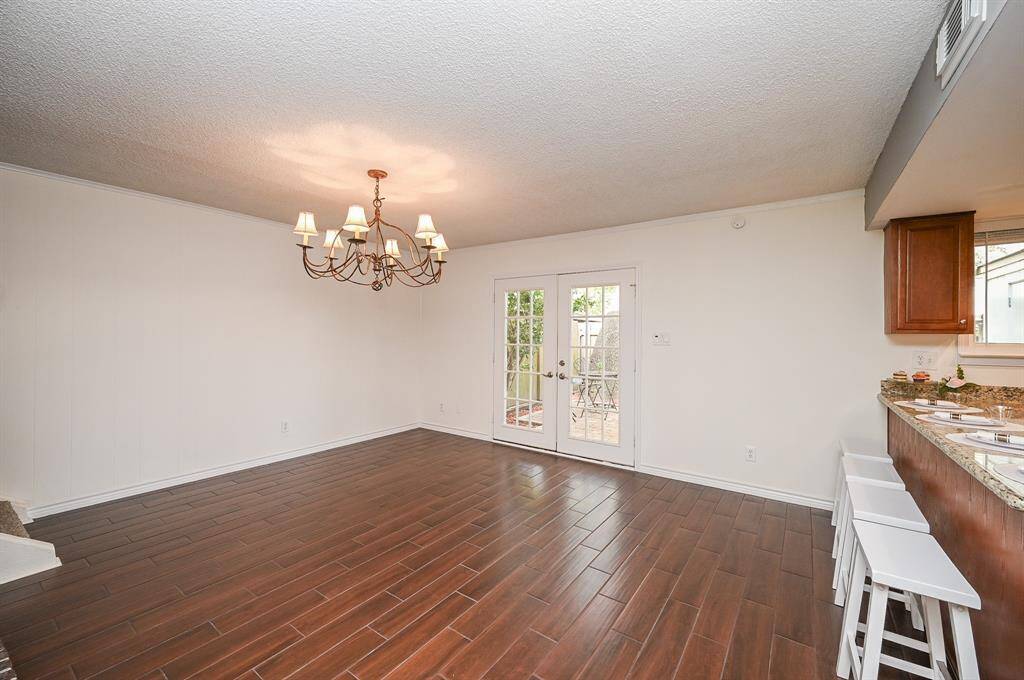 This spacious dining area features elegant wood flooring, a stylish chandelier, and French doors leading to an outdoor patio. The open layout connects seamlessly to the kitchen with a convenient breakfast bar.