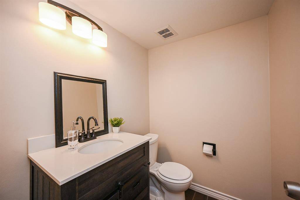 Modern half-bathroom with a sleek vanity featuring a dark wood finish, white countertop, and contemporary faucet. It includes a mounted mirror, toilet, and overhead lighting, creating a clean and inviting space.