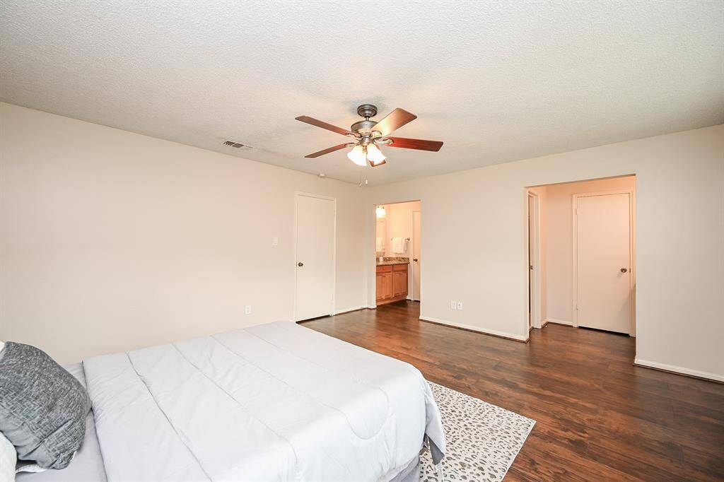 This spacious bedroom features hardwood floors, neutral walls, and a ceiling fan. It offers an ensuite bathroom with visible vanity, providing convenience and comfort.