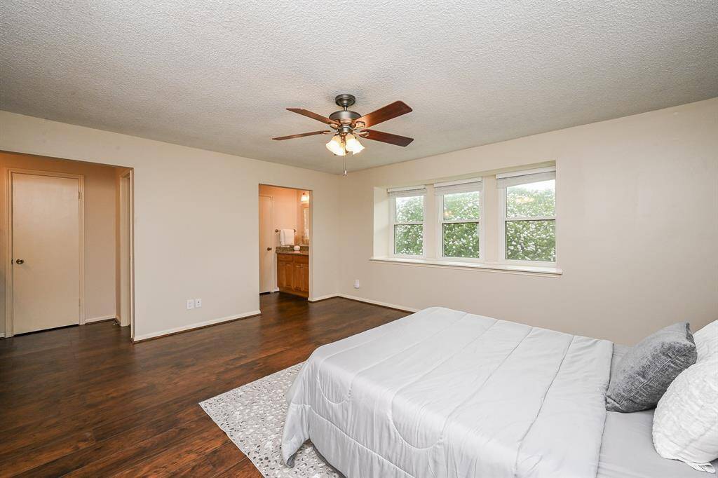 Spacious bedroom with hardwood floors, a ceiling fan, and ample natural light from large windows. The room features a cozy layout with an attached bathroom for convenience.