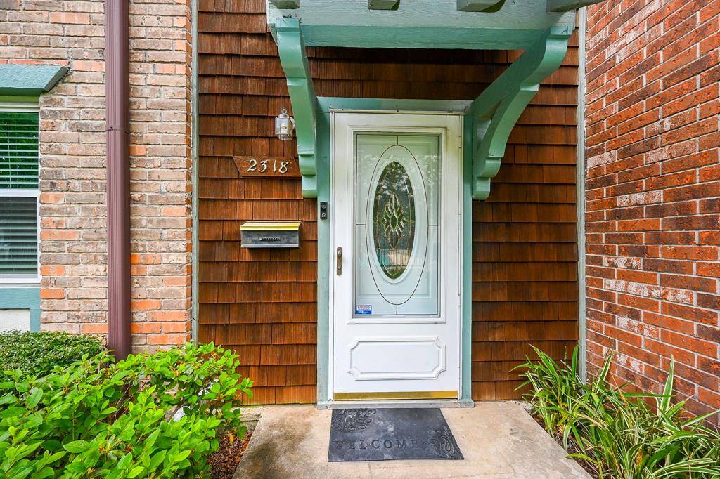 This inviting entrance features a beautifully maintained exterior with charming brick accents and lush landscaping, creating a warm welcome home.