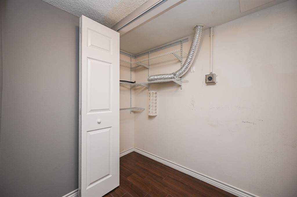 This photo shows a small utility room with wood flooring, featuring wire shelving and a flexible duct. It's compact with a neutral color scheme, suitable for storage or laundry use.