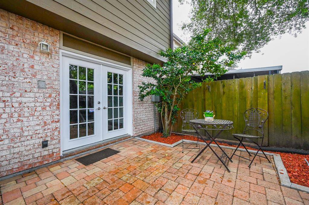 Charming patio with brick paving, featuring French doors, and a small garden area with a tree, perfect for outdoor relaxation.