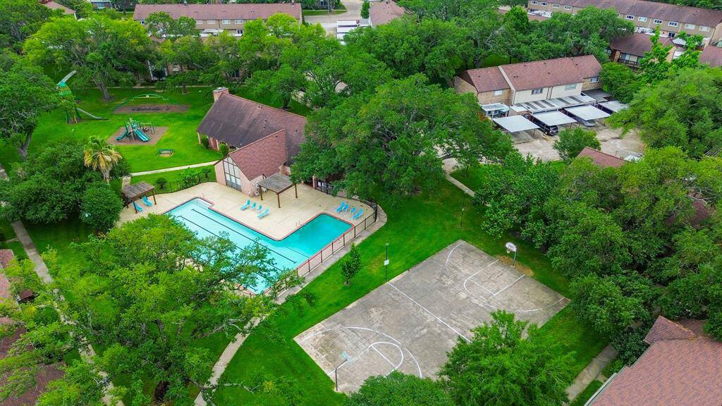 This photo showcases a community area with a large swimming pool, adjacent playground, and basketball court, surrounded by lush greenery and residential buildings, offering a family-friendly environment.