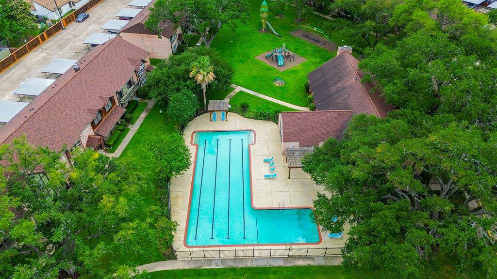 This property features a spacious outdoor area with a large swimming pool and a playground, surrounded by mature trees for added privacy. The community includes several buildings with convenient access to parking and lush green spaces.
