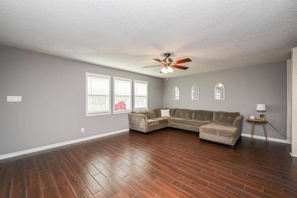 Spacious living room with elegant wood-look tile flooring, neutral gray walls, and ample natural light from multiple windows.