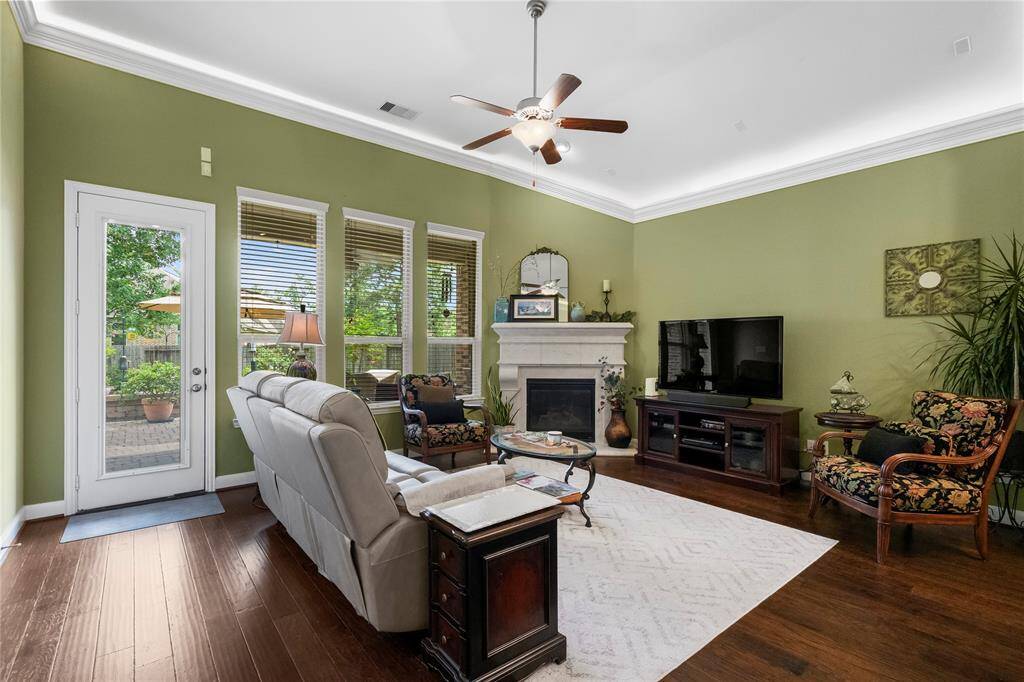 Bright and inviting living room with green walls, featuring a cozy fireplace, ceiling fan, and hardwood floors. Large windows and a glass door provide plenty of natural light and access to a patio.