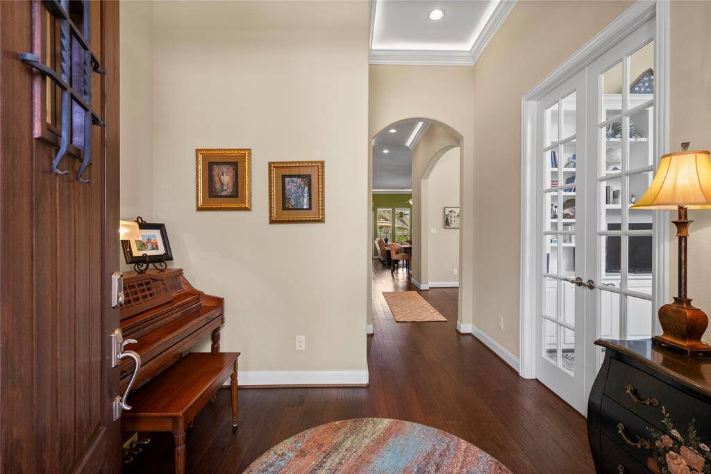 This welcoming entryway features warm wooden flooring, with enough space for a classic piano, and elegant decor. French doors open into a bright room, while an arched hallway leads to a cozy living area.