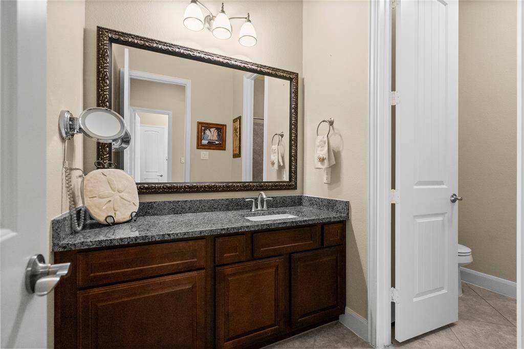 This photo showcases a stylish bathroom with a granite countertop, dark wood cabinetry, a large framed mirror, elegant lighting, and a privacy door.