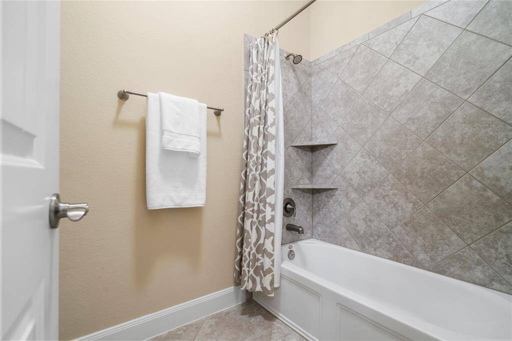 This bathroom features a clean, modern design with a tiled shower and bathtub combo. It includes neutral tones, a patterned shower curtain, and convenient wall shelving.