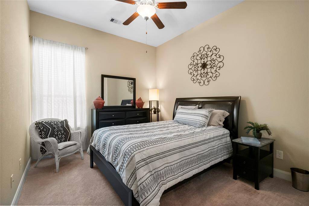 This cozy bedroom features a warm, neutral color scheme with a large window allowing natural light. It includes a stylish ceiling fan, creating a welcoming and relaxing atmosphere.