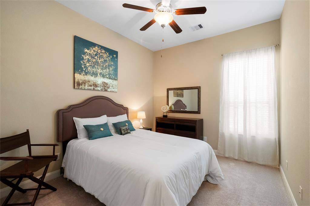 This cozy bedroom features neutral walls, a ceiling fan, and soft carpeting. Natural light filters through the sheer curtains, creating a warm and inviting atmosphere.