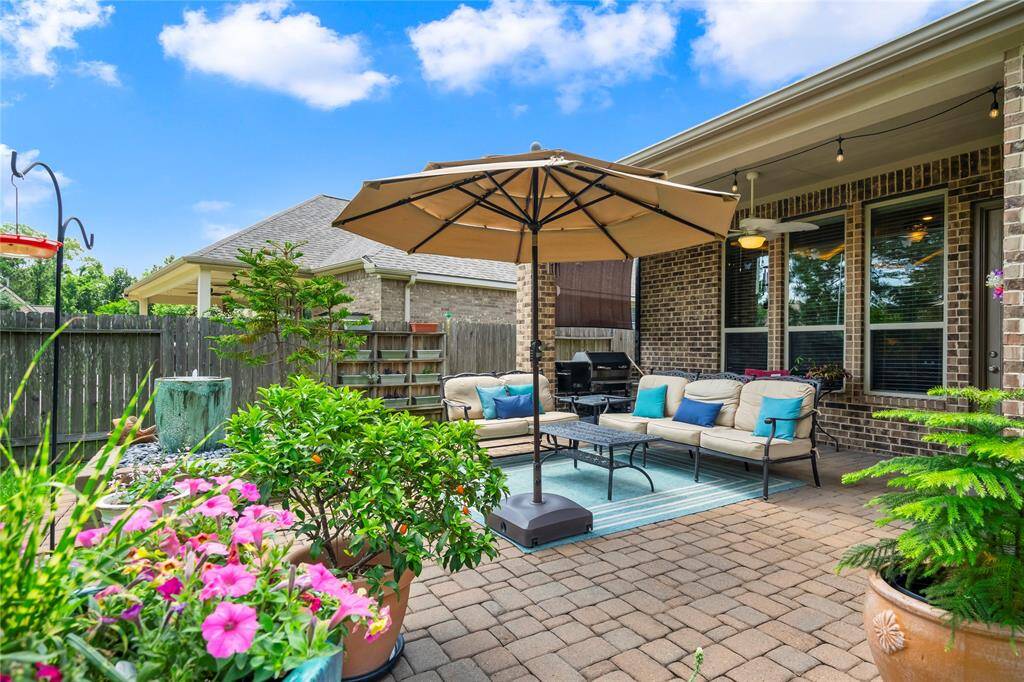 This inviting backyard patio features a cozy seating area with cushioned furniture under a large umbrella, surrounded by vibrant potted plants and a well-maintained brick exterior. Ideal for outdoor relaxation and entertaining.
