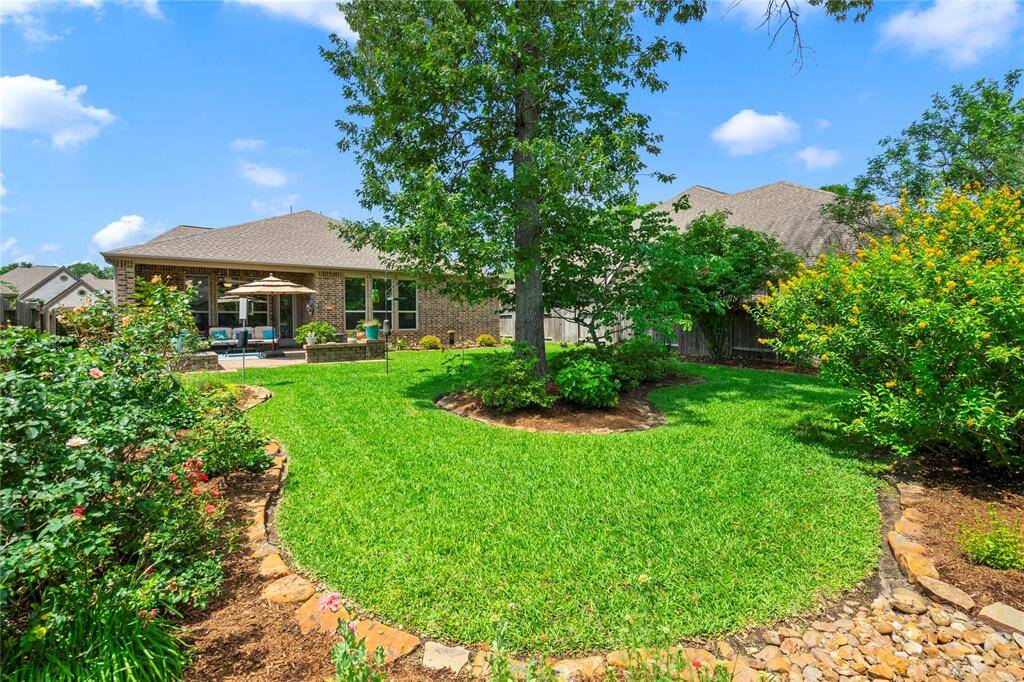This photo showcases a charming backyard with a well-maintained lawn, mature trees, and colorful plants. There is a spacious patio with comfortable seating and an umbrella, perfect for outdoor relaxation and entertaining.