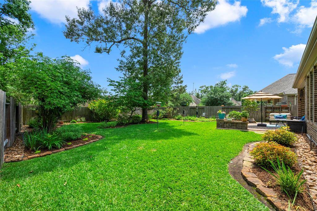This backyard offers a spacious, lush lawn with well-maintained landscaping, mature trees, and a cozy patio area perfect for relaxation and entertaining.