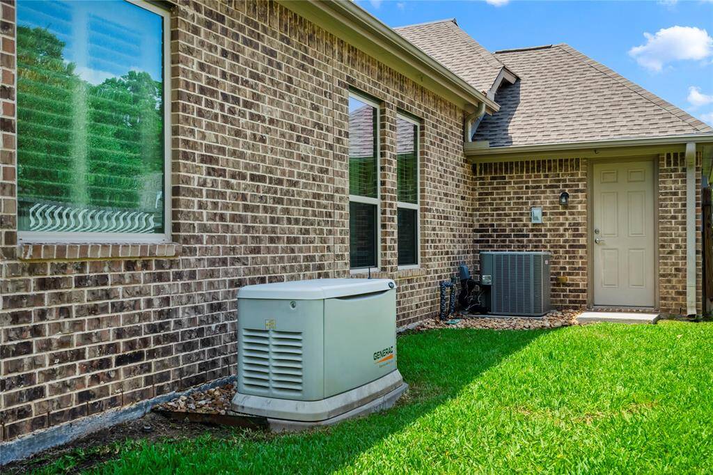 The photo shows the side of a brick house with a well-maintained lawn. It features a backup generator and an air conditioning unit near a side entrance, highlighting practical utility installations.